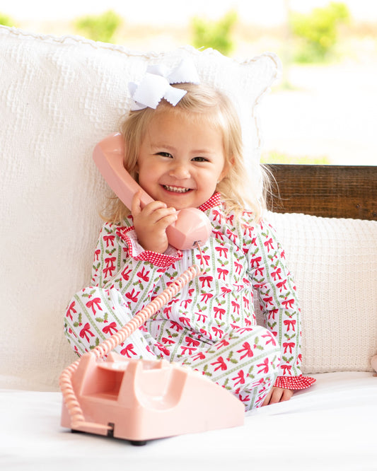 Child wearing a festive outfit with a pink phone, sitting on a white couch outdoors.
