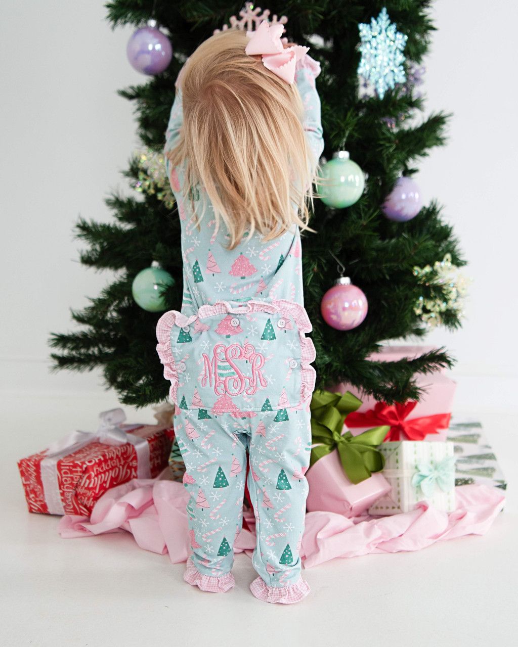 Child wearing a festive pajama set in front of a decorated Christmas tree.