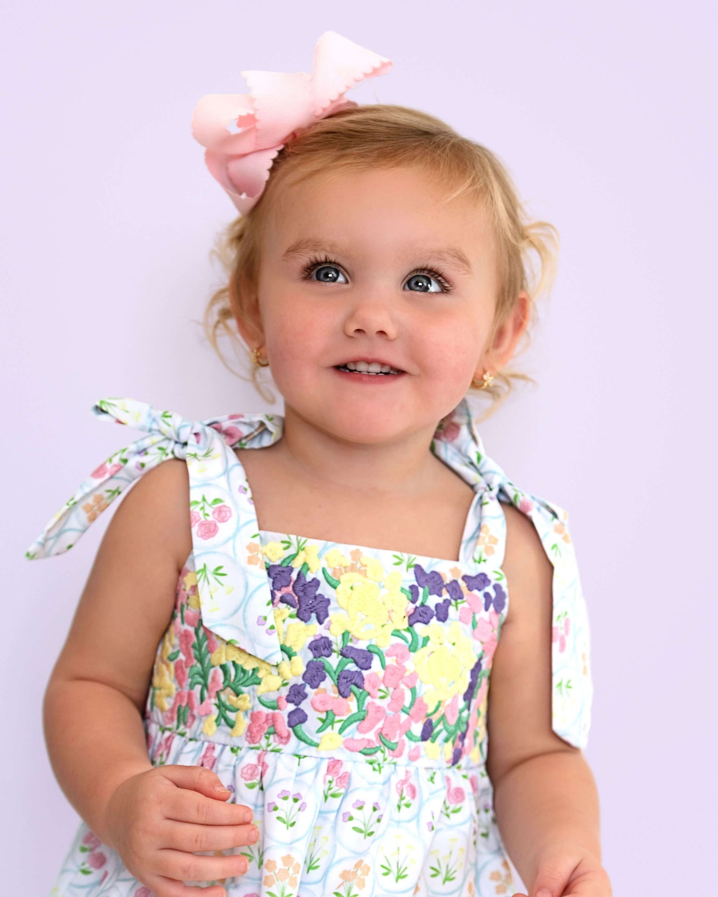 Child wearing a floral bubble with a large bow on a light purple background