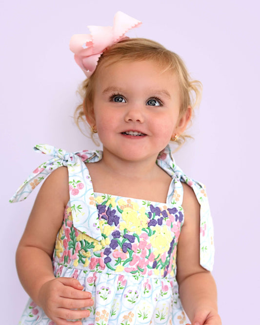 Child wearing a floral bubble with a large bow on a light purple background