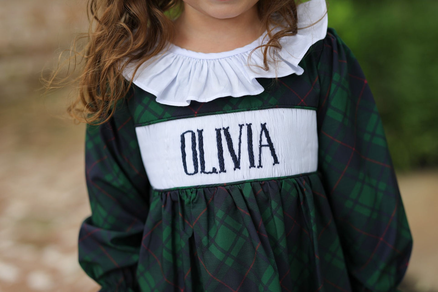 Child wearing a green plaid dress with a white collar and 'OLIVIA' nameband.