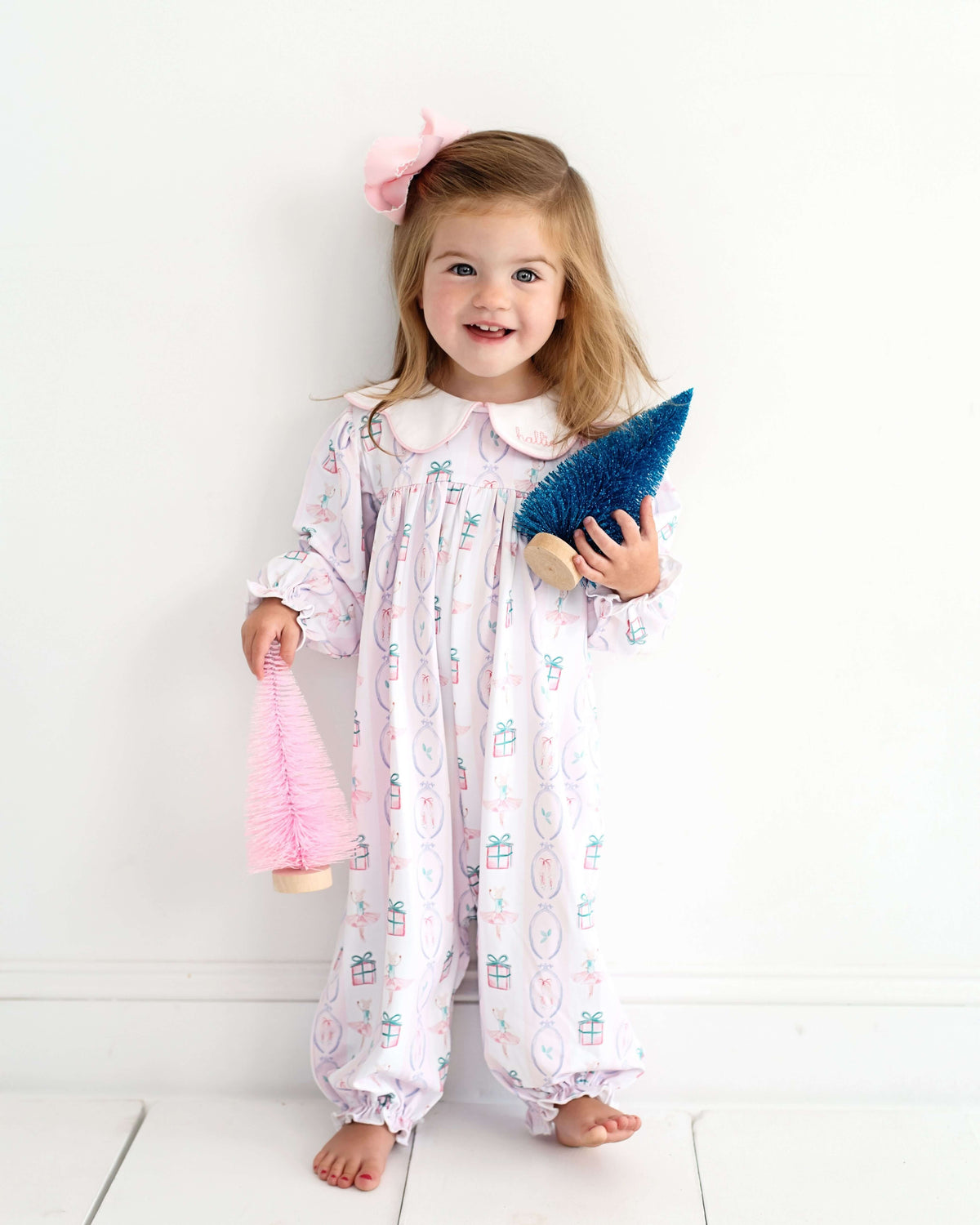 Child_wearing_a_holiday_patterned_long_bubble_holding_a_pink_and_blue_Christmas_tree_in_each_hand_on_a_white_background_1_1
