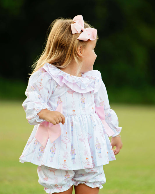 Child wearing a light blue and pink holiday nutcracker outfit with pink accents outdoors.