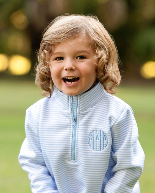 Child wearing a light blue and white striped pullover with a monogram, standing outdoors.