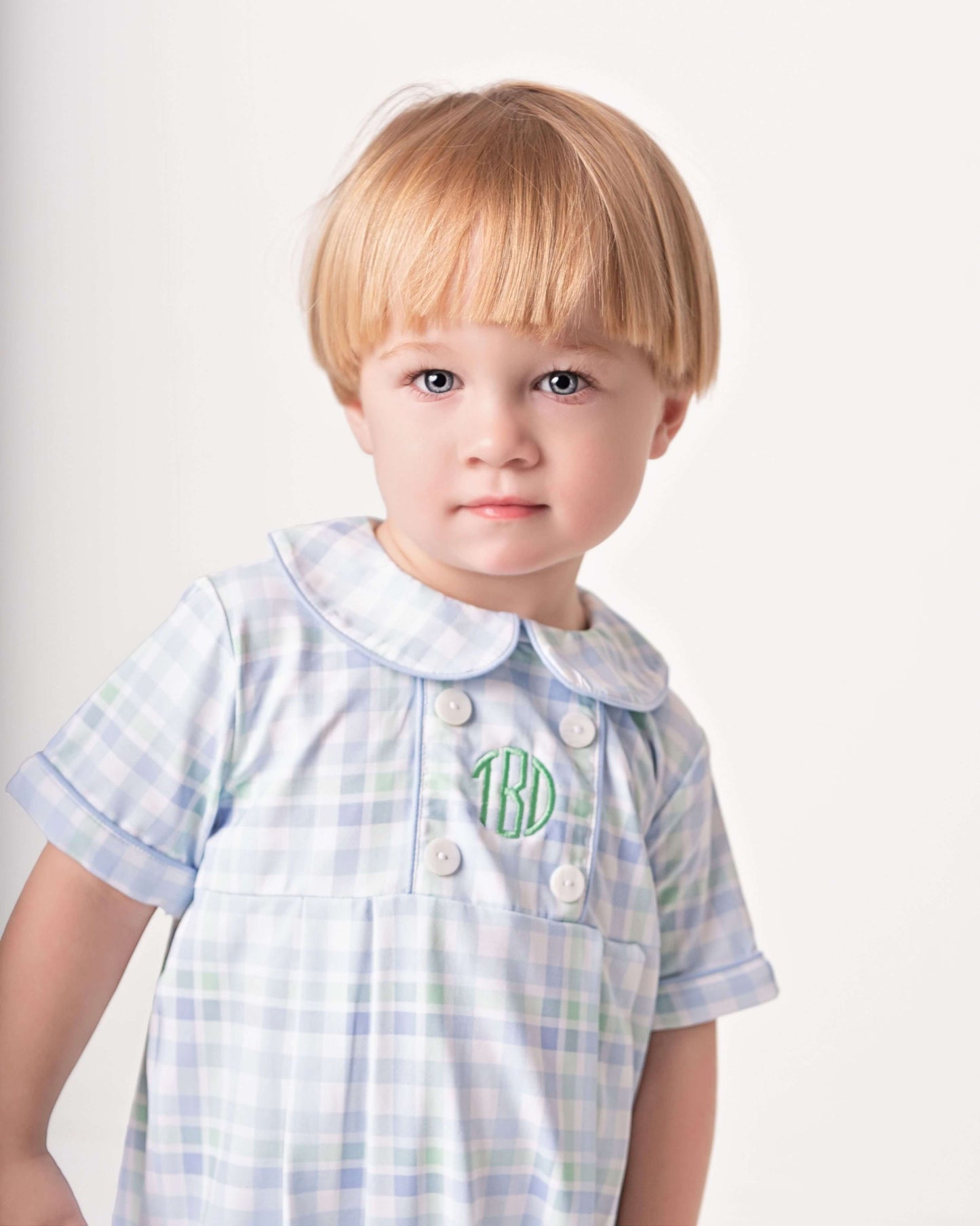 Child wearing a light blue checkered dress with white buttons on a plain background