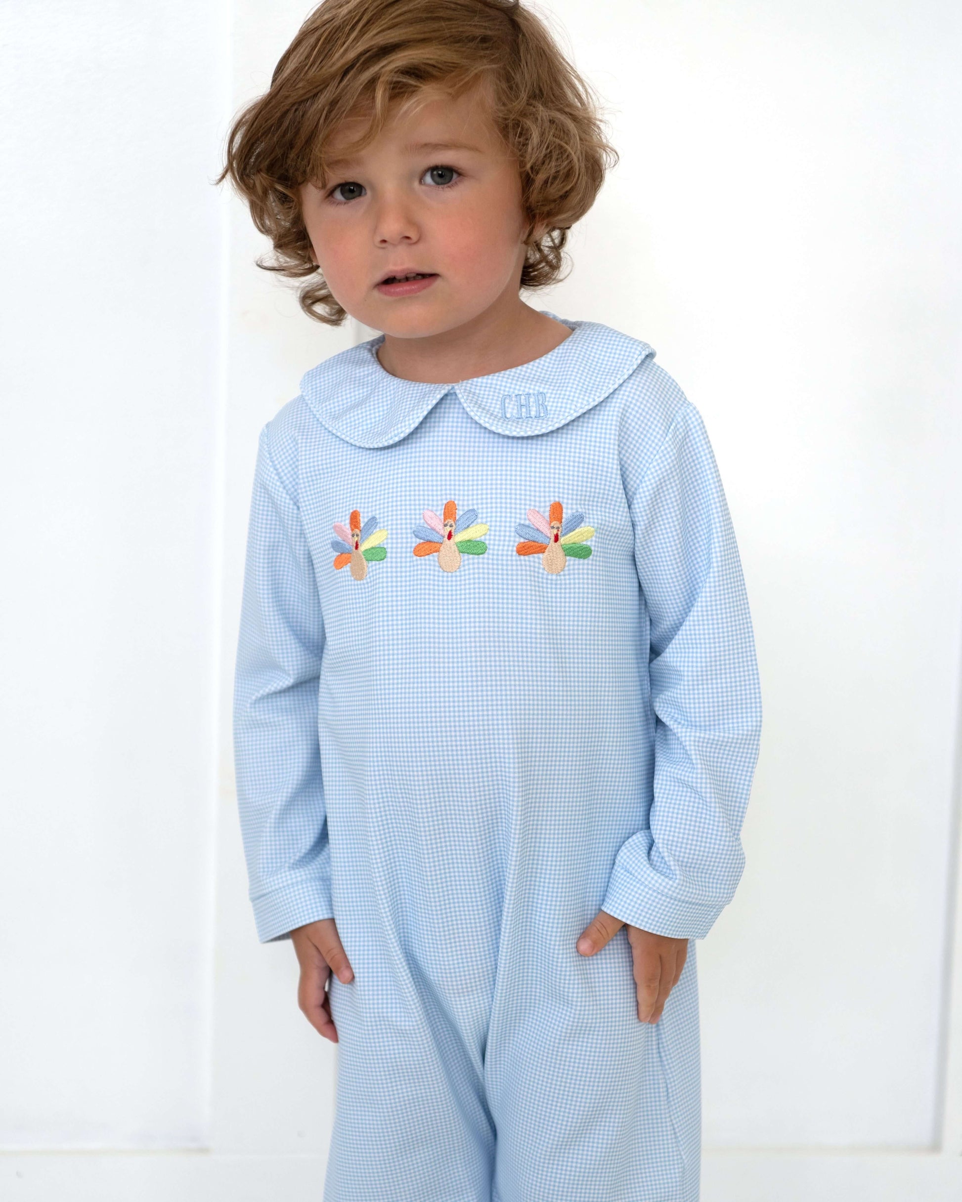 Child wearing a light blue checkered outfit with embroidered flowers on a white background