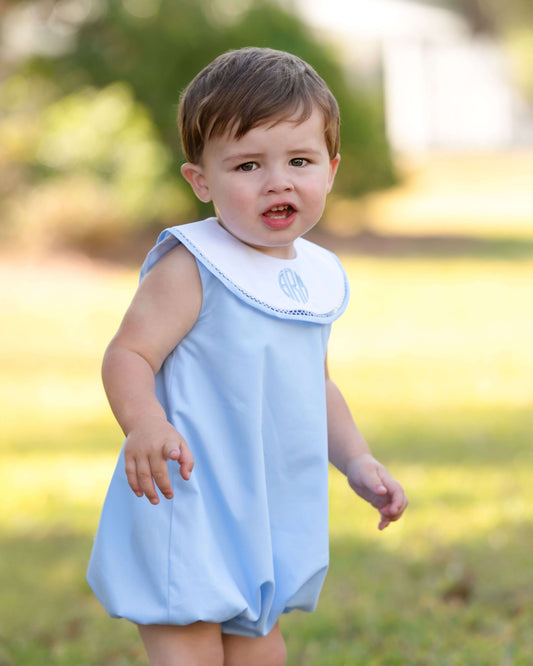 Child wearing a light blue dress with a white collar in an outdoor setting