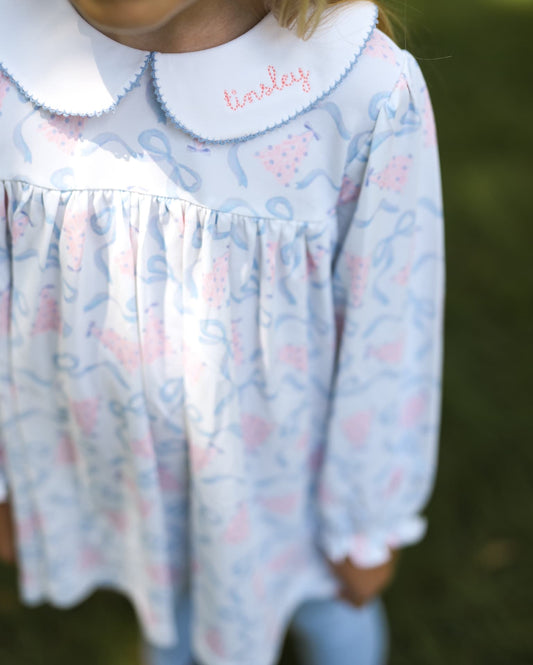 Child wearing a light blue dress with floral pattern and white collar, standing outdoors.