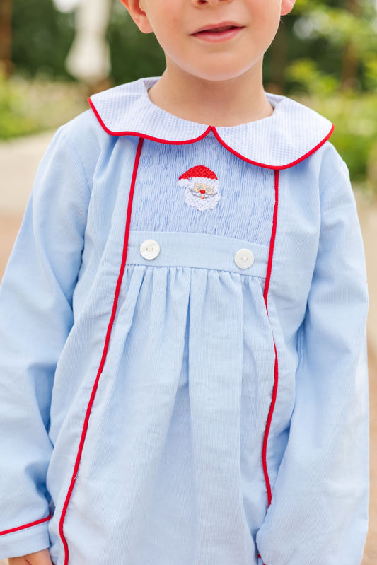 Child wearing a light blue dress with red trim and a embroidered design outdoors.