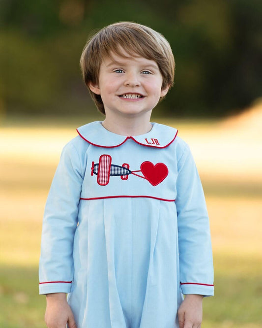 Child wearing a light blue dress with red trim and heart design outdoors.