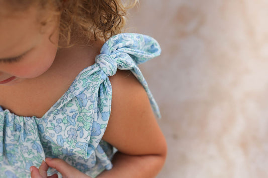 Child wearing a light blue floral dress with a bow detail on a blurred background