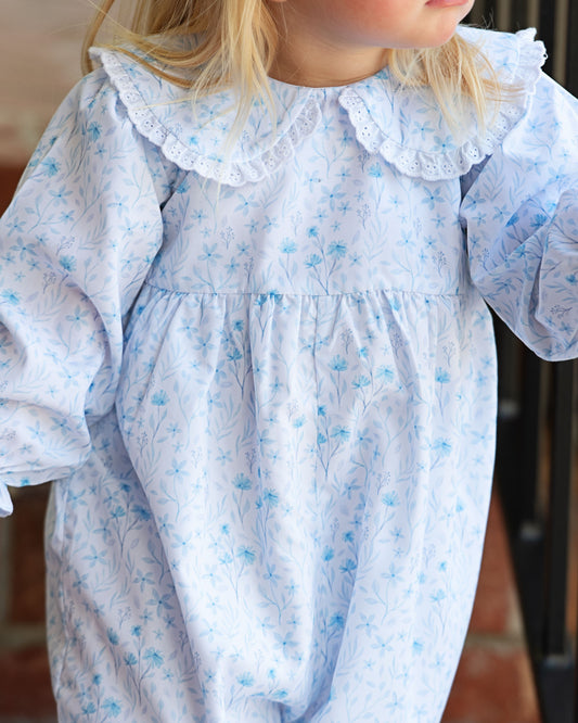Child wearing a light blue floral dress with a ruffled collar.