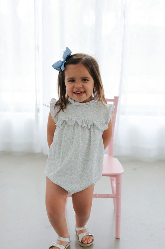Child wearing a light blue floral romper with a white background