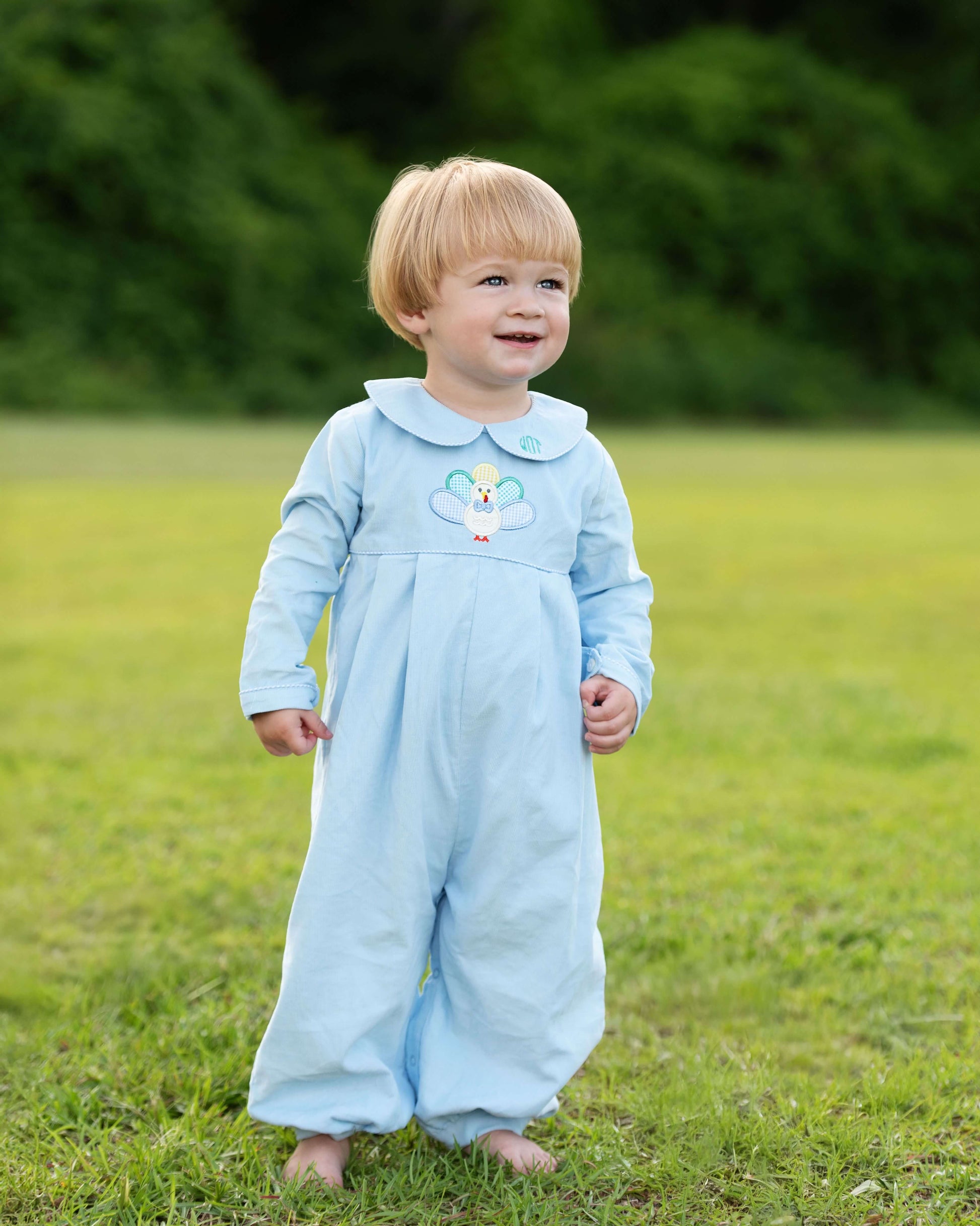 Child wearing a light blue outfit with a cartoon character on a grassy field