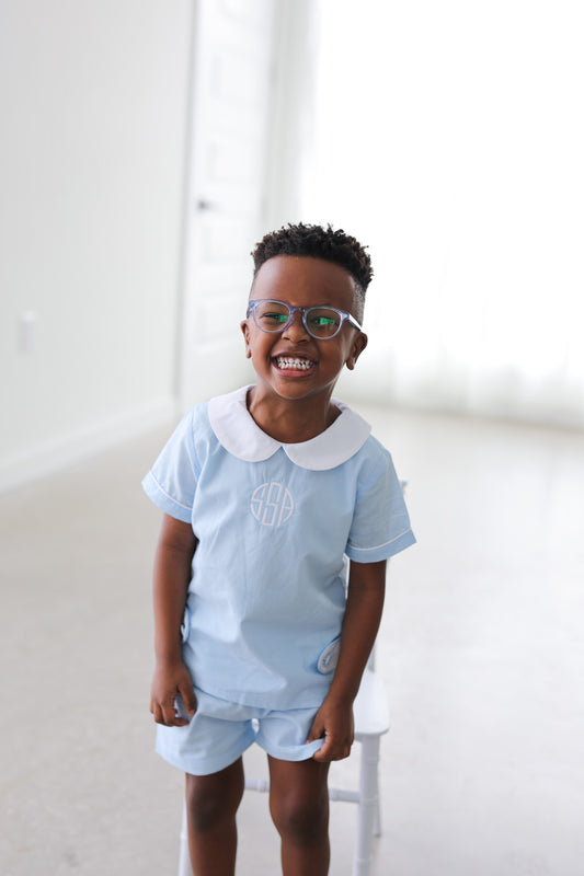 Child wearing a light blue outfit with a white collar, standing against a white background