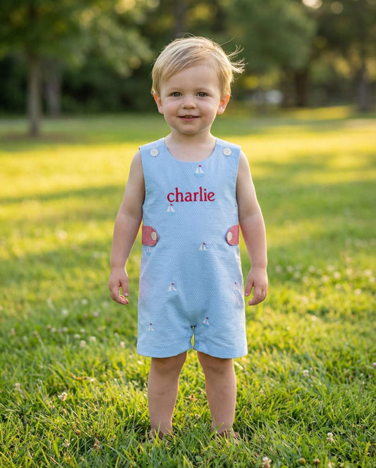 Child wearing a light blue romper with 'charlie' printed on it, standing in a grassy field.