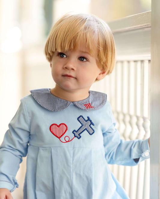 Child wearing a light blue romper with decorative elements, standing indoors.