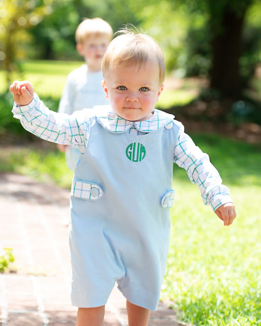 Child wearing a light blue romper with green monogram outdoors