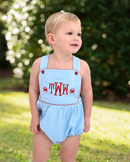Child wearing a light blue romper with red text and crab designs outdoors.