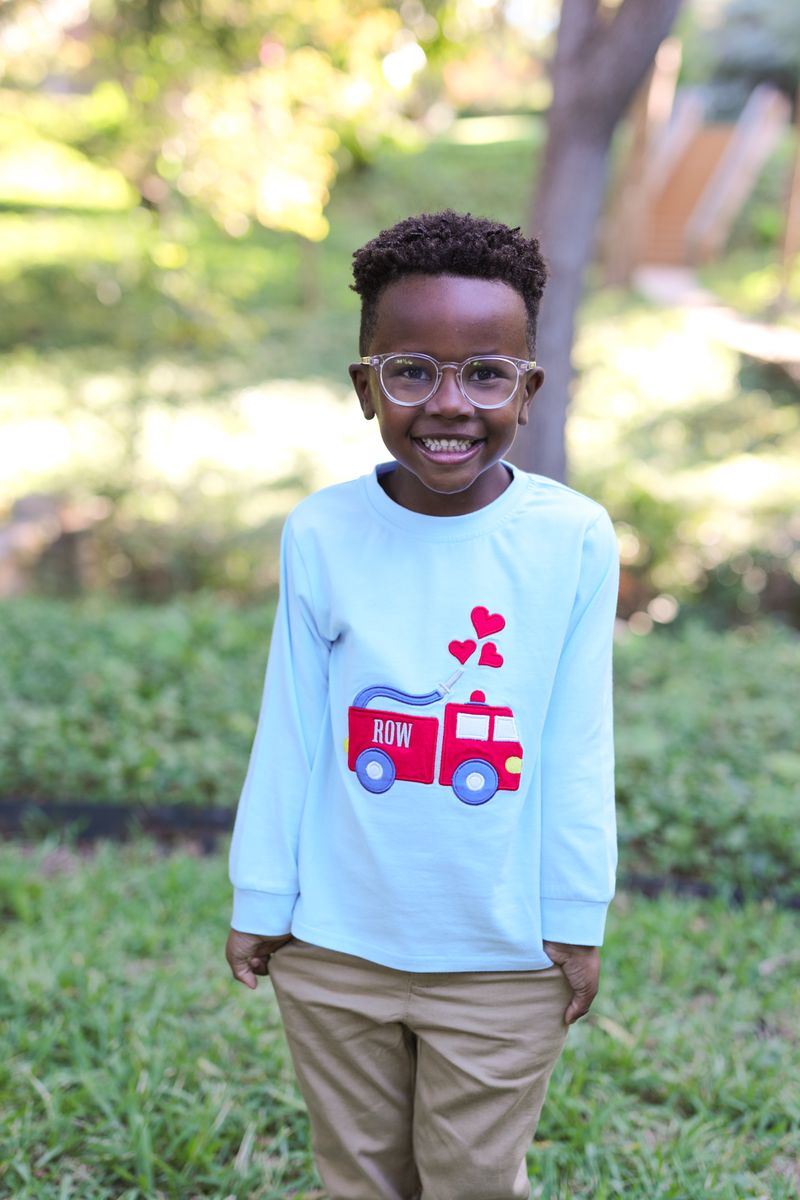 Child wearing a light blue shirt with a red fire truck design outdoors