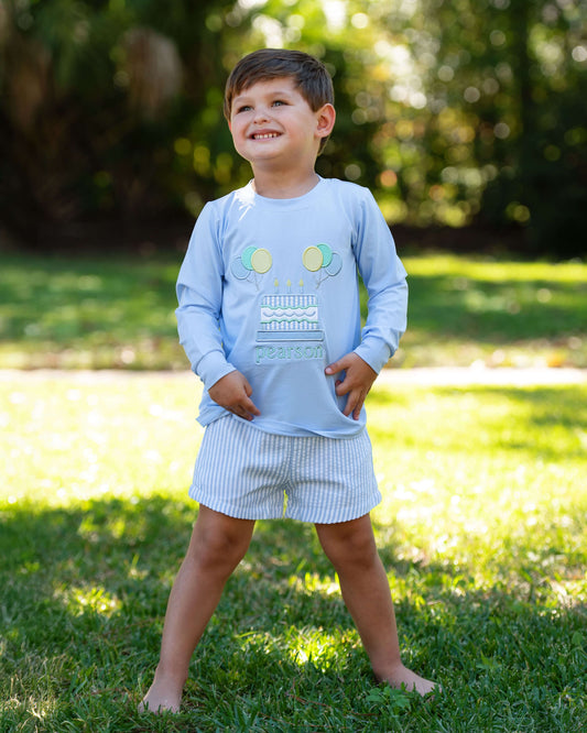 Child wearing a light blue shirt with a robot design and shorts outdoors on grass