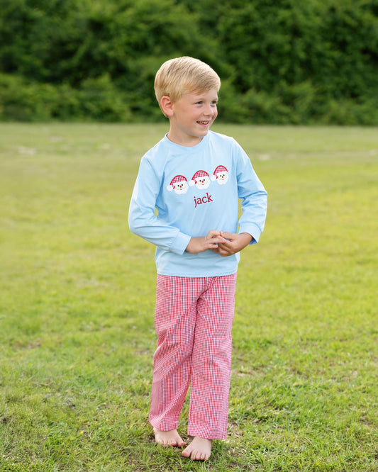 Child wearing a light blue shirt with a snowman design and pink checkered pants standing in a grassy field.
