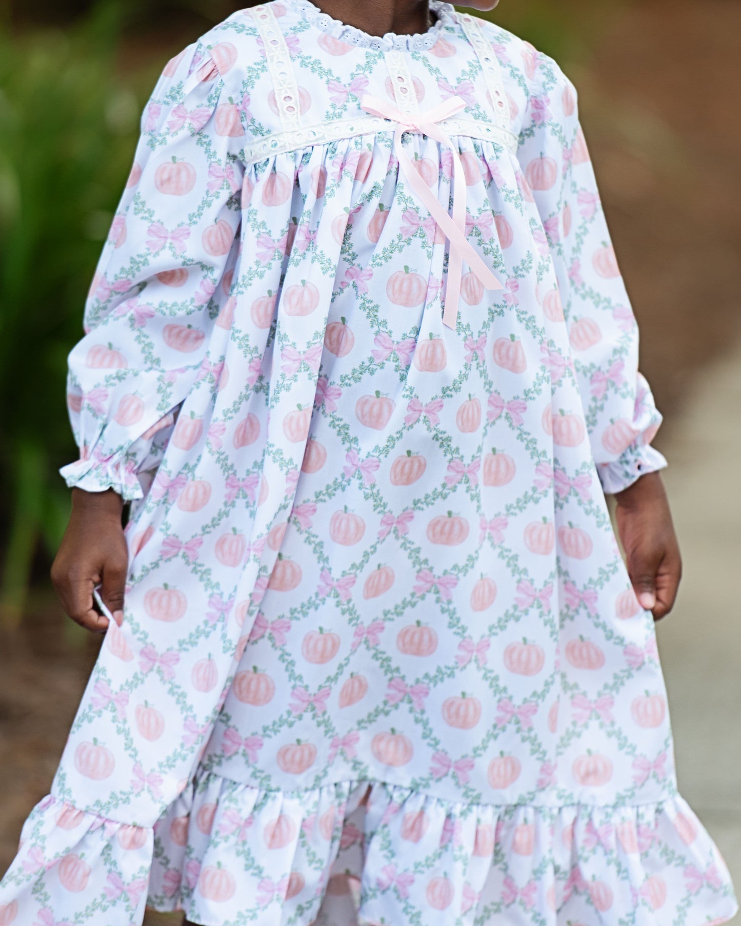 Child wearing a long-sleeve night gown with pink pumpkins on a light blue background.