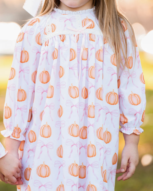 Child wearing a nightgown with orange pumpkin pattern against a blurred outdoor background