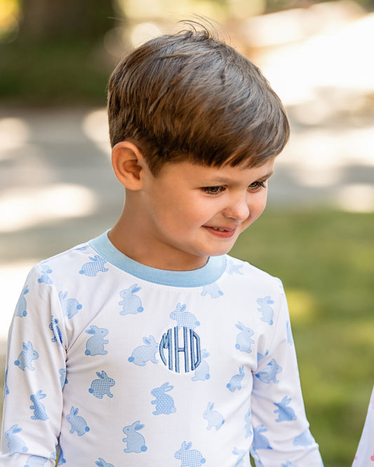 Child wearing a pajama top with bunny patterns and a monogram, standing outdoors.