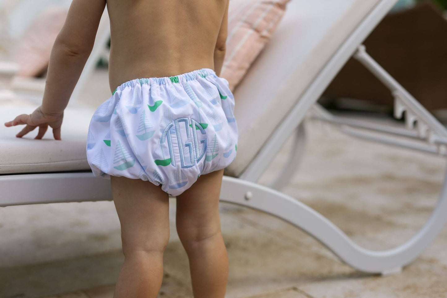 Child wearing a patterned diaper sitting on a lounge chair.