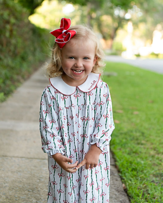 Child wearing a patterned dress with a red bow in a park setting