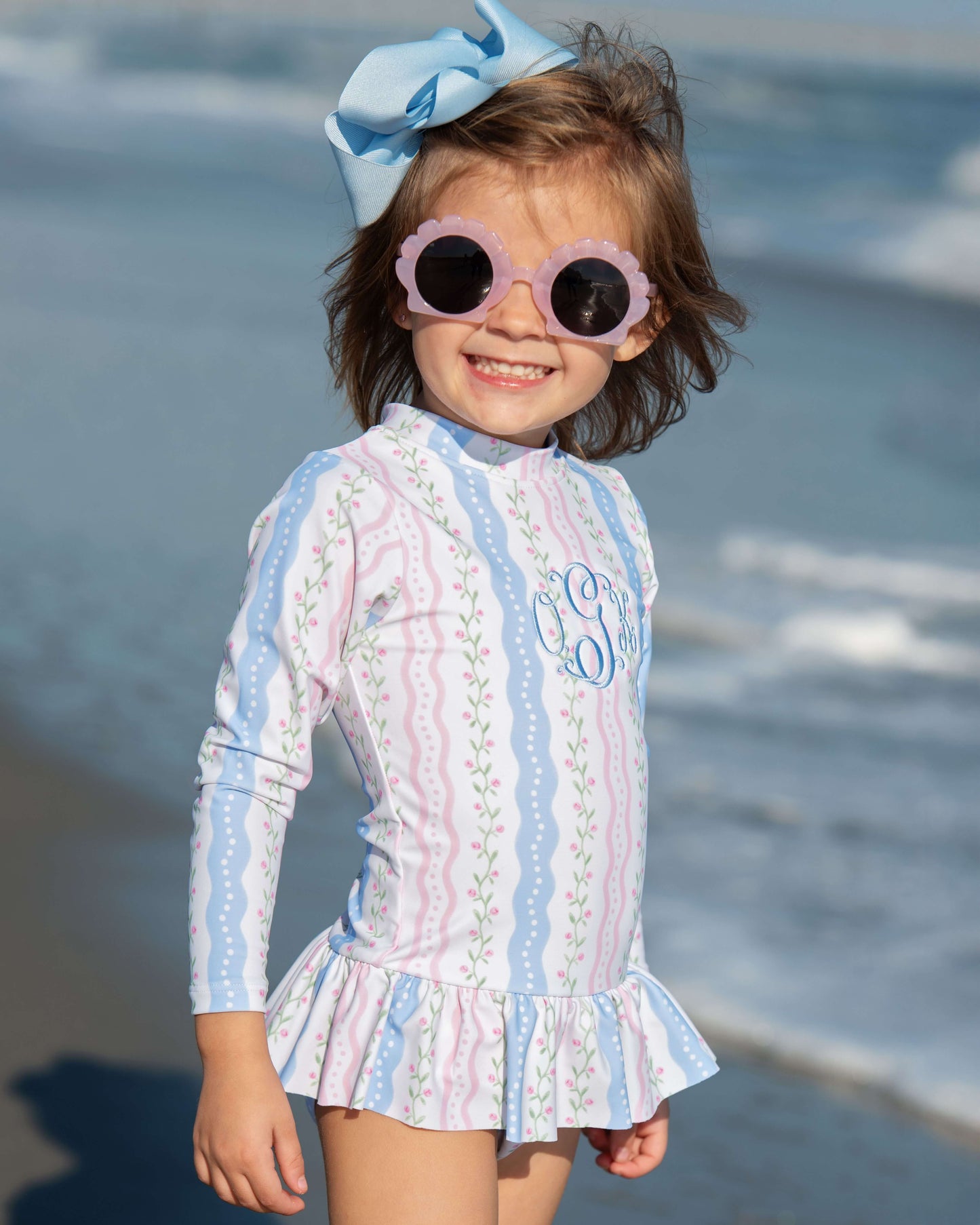 Child wearing a patterned outfit with sunglasses on a beach