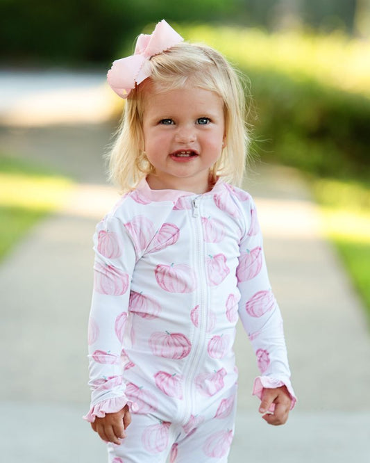 Child wearing a pink and white patterned outfit with a bow in a park setting