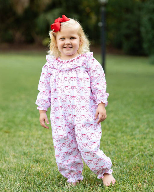 Child wearing a pink and white patterned outfit with a red bow in a grassy outdoor setting
