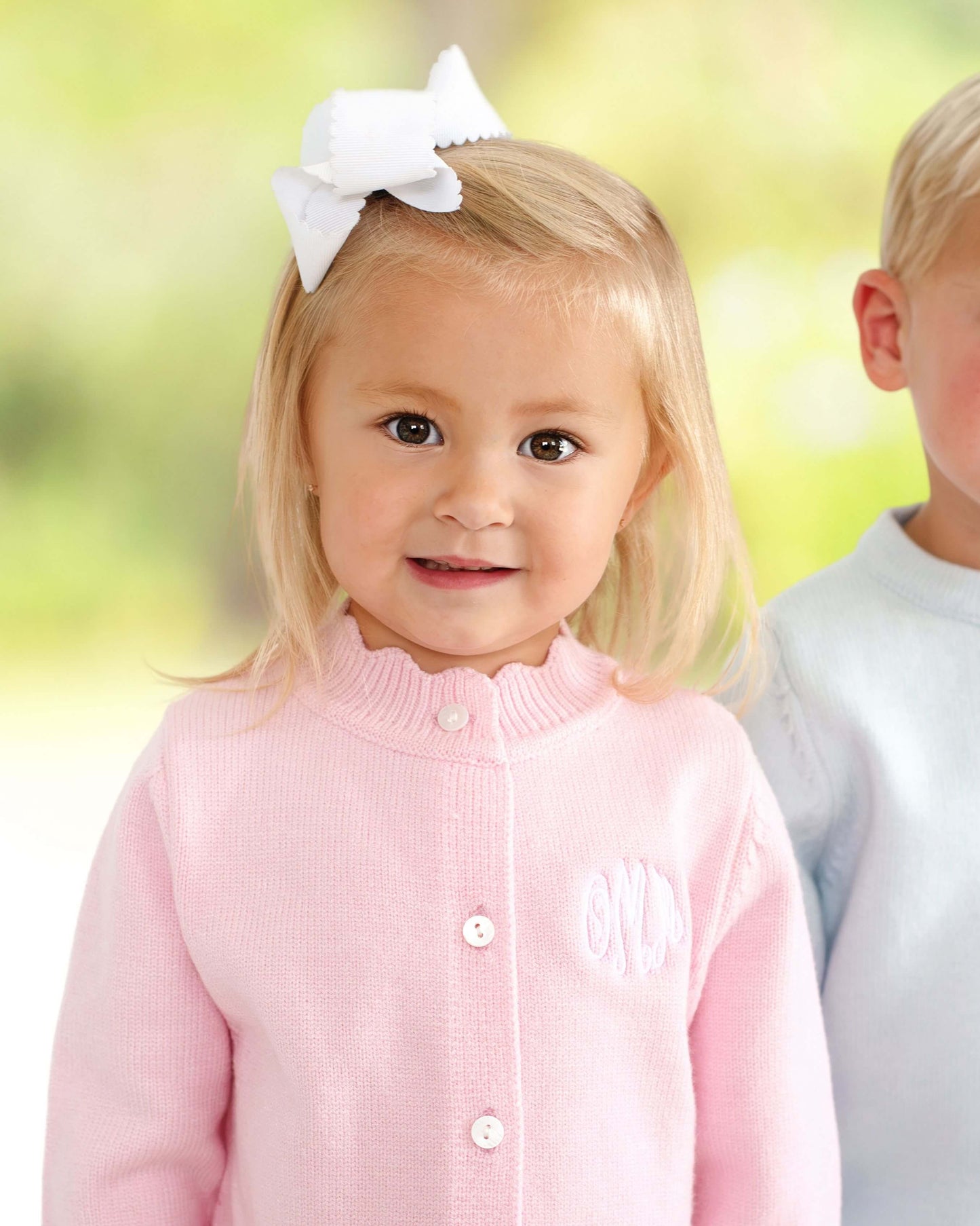 Child wearing a pink cardigan, standing outdoors with a blurred background.