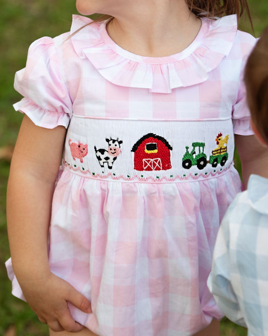 Child wearing a pink dress with farm-themed embroidery outdoors