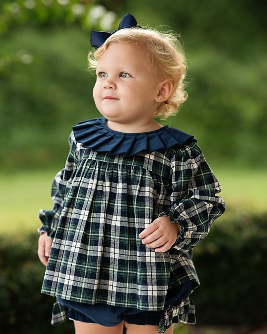 Child wearing a plaid diaper set with a navy bow in an outdoor setting