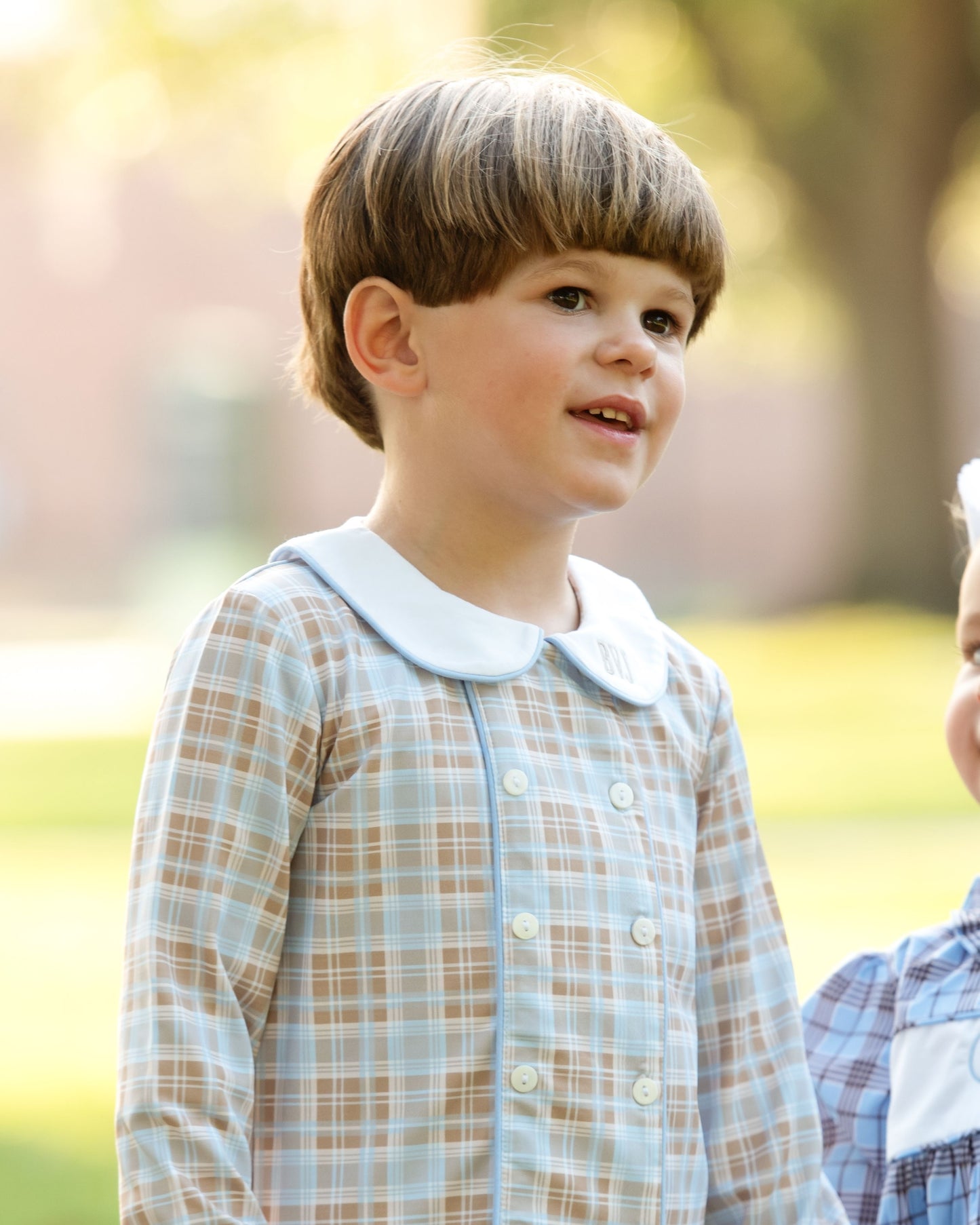 Child wearing a plaid dress with a blurred outdoor background