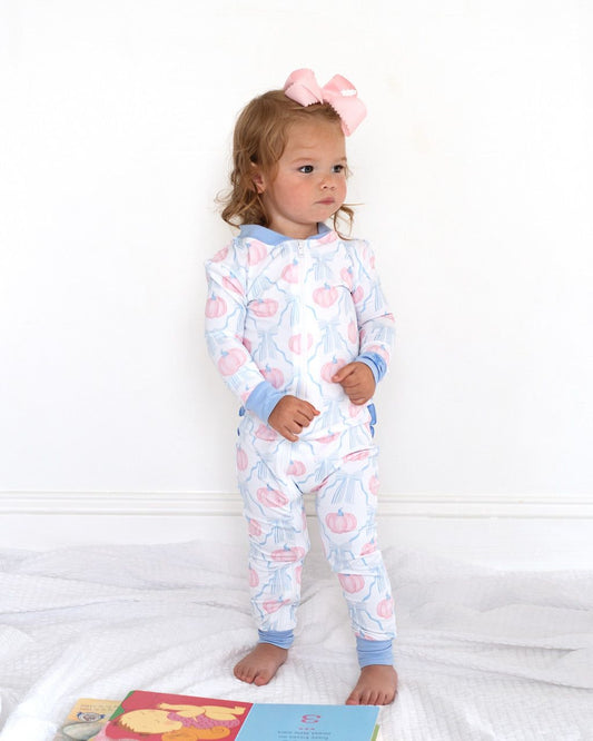 Child wearing a pumpkin patterned zipper pajama with a pink bow on a white background