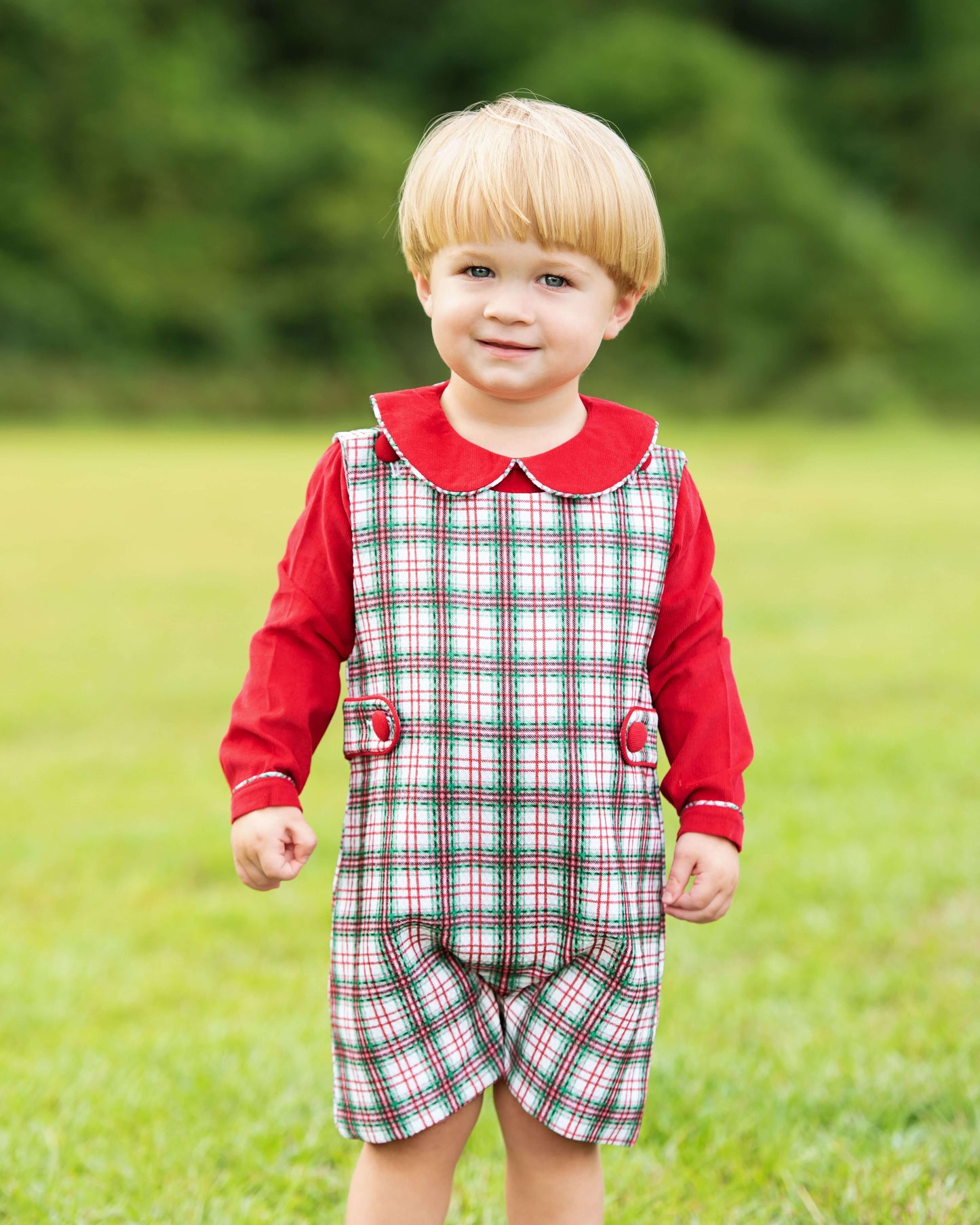 Child wearing a red and green checkered dress with a red collar in an outdoor setting
