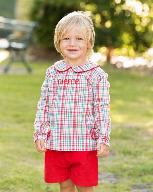 Child wearing a red and green checkered shirt with 'Pierce' on it, standing outdoors.