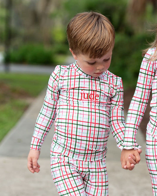 Child wearing a red and green plaid outfit with 'jude' printed on it, standing outdoors.