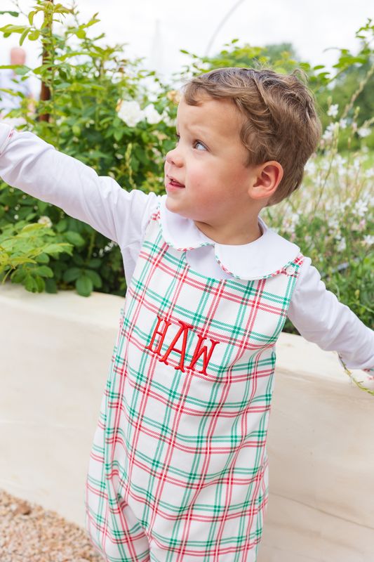 Child wearing a red and green plaid romper with 'HAW' on it, standing outdoors.
