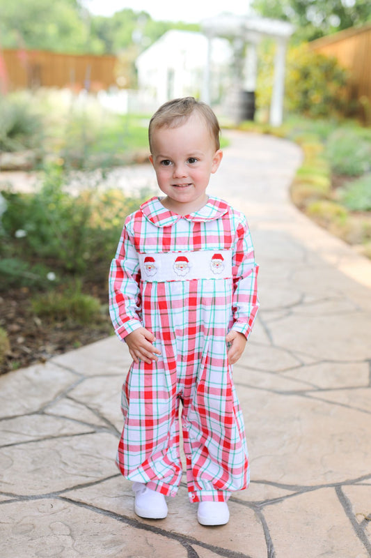 Child wearing a red and white checkered outfit with a Santa face on a stone path outdoors.