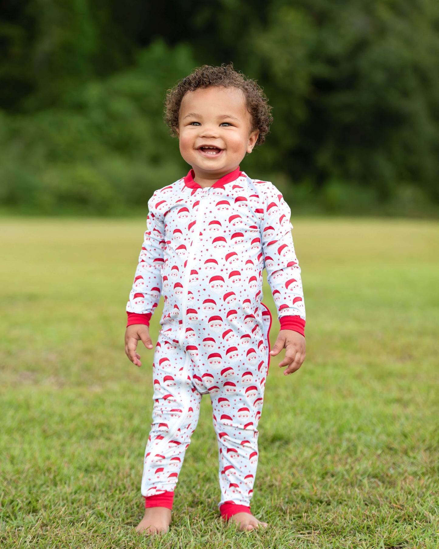 Child wearing a red and white patterned onesie standing in a grassy field.