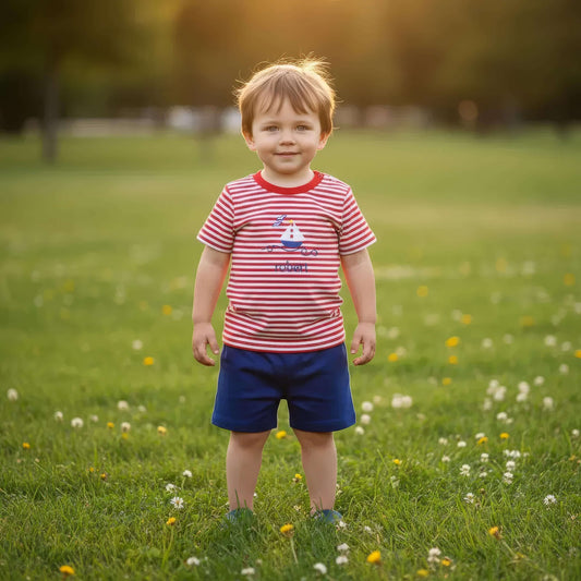 Child wearing a red and white striped shirt and blue shorts standing in a grassy field with flowers.