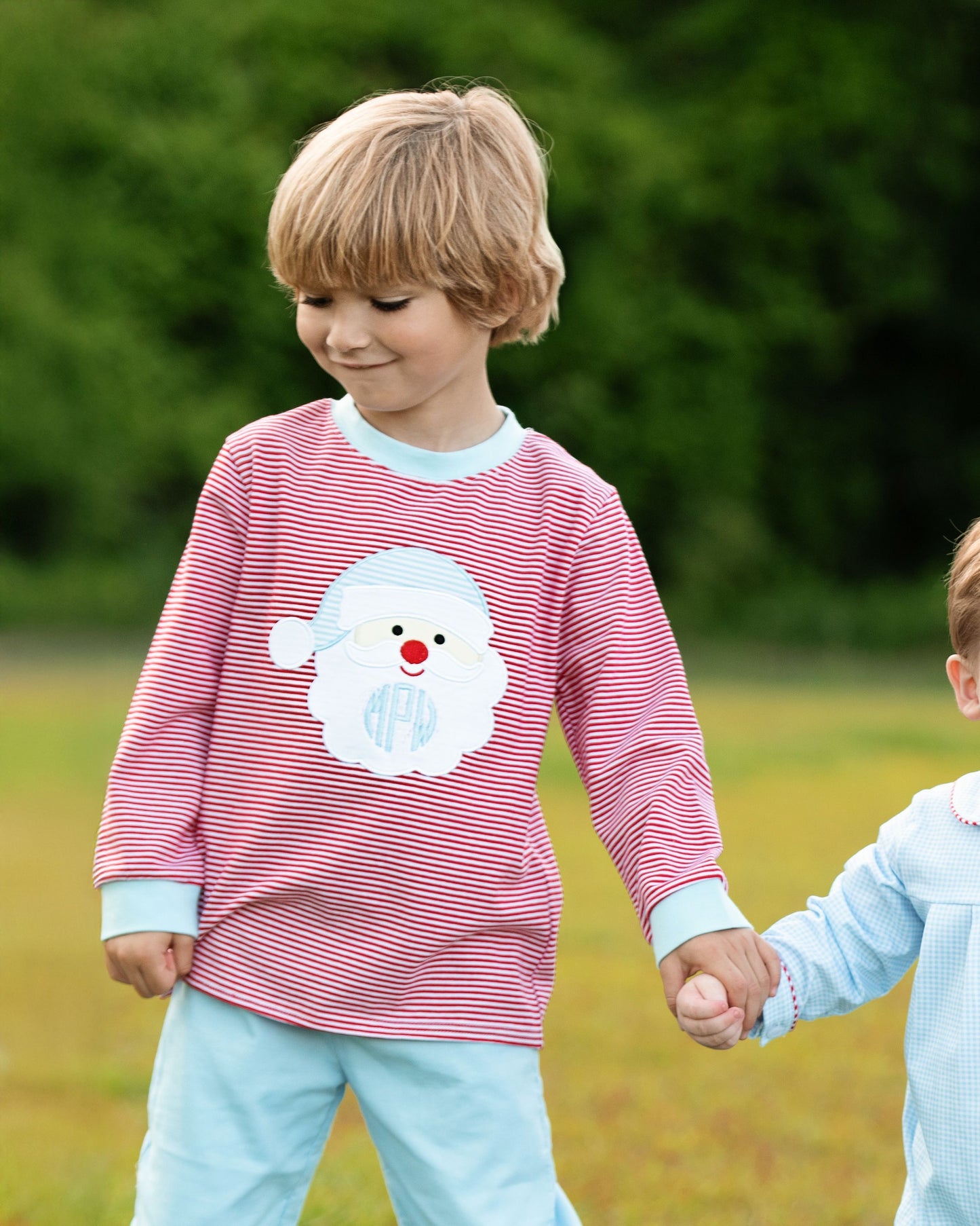 Child wearing a red and white striped shirt with a snowman design, standing outdoors.