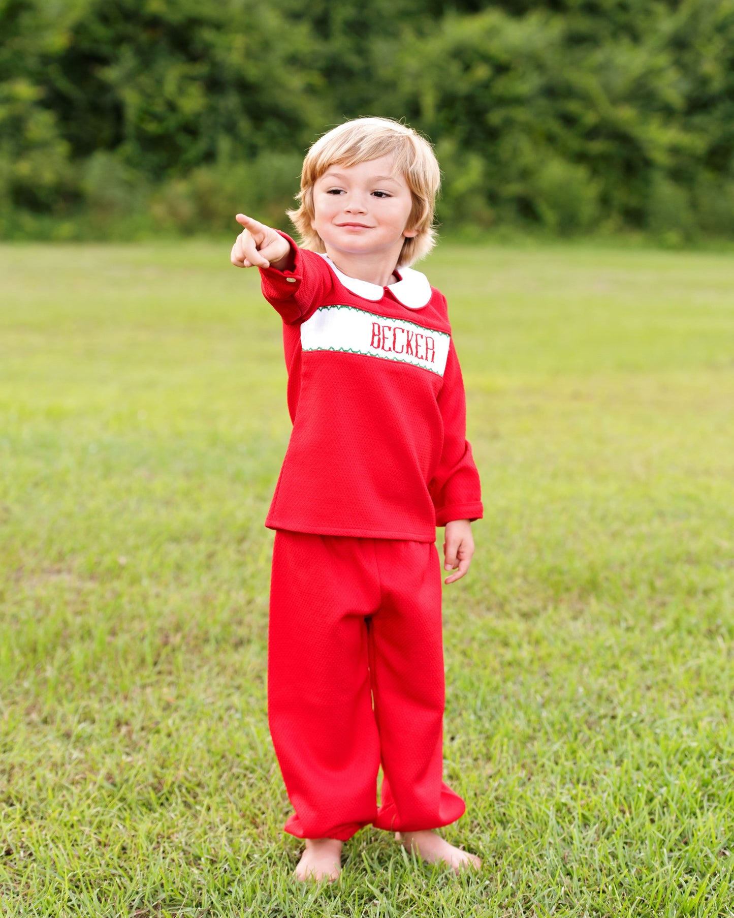 Child wearing a red outfit with 'Believer' text, standing in a grassy field.