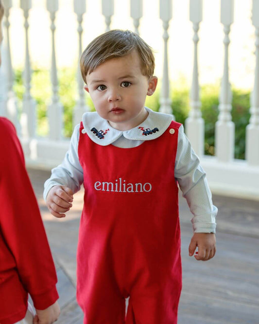 Child wearing a red outfit with 'emiliano' printed on it, standing outdoors.