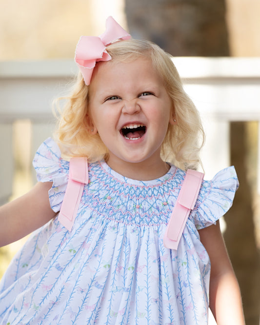 Child wearing a smocked dress with pink bows outdoors